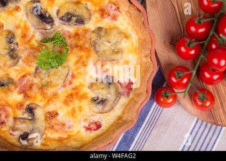 In casa gustosi quiche nel piatto di terracotta, con legno di ulivo tagliere e ciliegia pomodori a grappolo Foto Stock