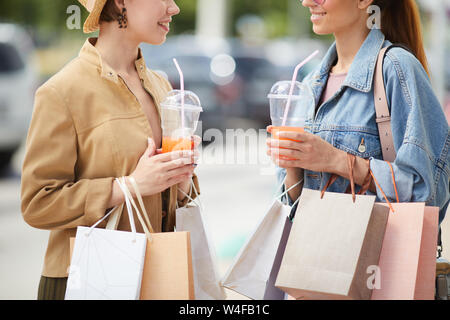 Close-up di ragazze eleganti in abiti casual in piedi sul parcheggio auto e di bere succo di frutta dopo lo shopping Foto Stock