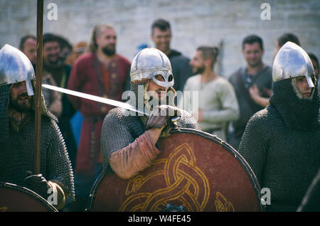 Staraya Ladoga, San Pietroburgo, Russia - 22 Giugno 2019: Viking in mail a catena e con una visiera che tiene una spada sulla sua spalla tra due guerrieri Foto Stock