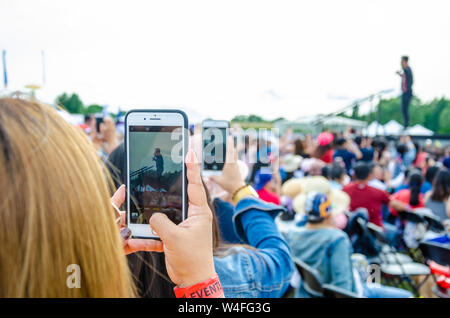 Un paio di lady di scattare delle foto di un attore su un palcoscenico usando i loro cellulari a un grande open air evento. Foto Stock