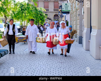 Zagabria, Croazia. Gruppo di persone vestite di bianco abiti tradizionali camminando sulla strada della città con le attività agricole e le attrezzature di cottura. Foto Stock