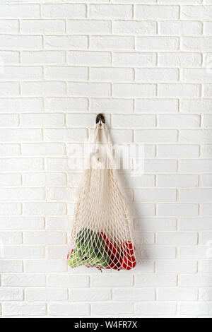 Cotone bianco borsa a rete con verdure appeso su whitewall. Plastica concetto libero Foto Stock