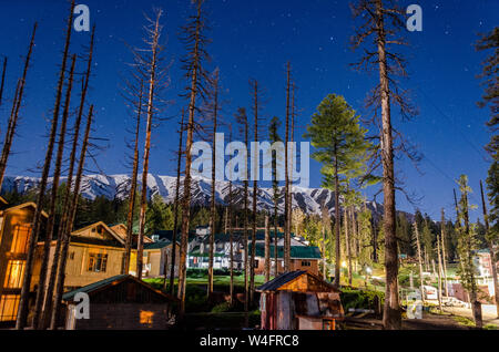 Vista notturna di Snow capped Pir Panjal gamma cercando su case e alberghi in mezzo ad alberi di pino a Gulmarg, Jammu e Kashmir India Foto Stock