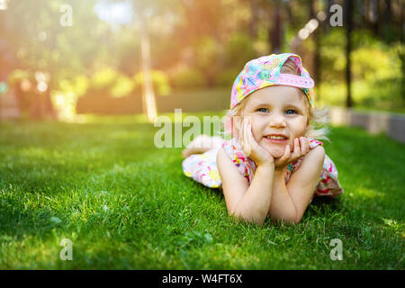 Bambina posa su erba verde con le mani sulle guance a casa cortile sulla soleggiata giornata estiva Foto Stock