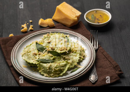 Deliziosi tortelli verdi con la salvia, il formaggio e i pinoli servita su tavoli in legno nero con forcella e igienico Foto Stock