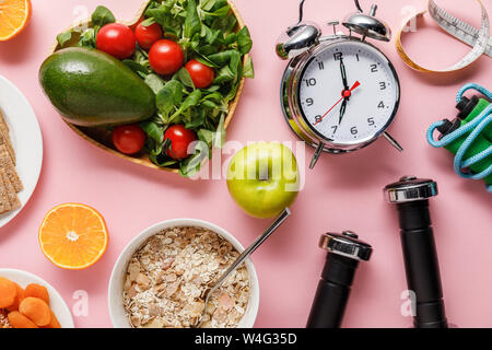 Vista superiore della dieta fresco cibo, nastro di misurazione, attrezzature sportive e sveglia su sfondo rosa con spazio di copia Foto Stock