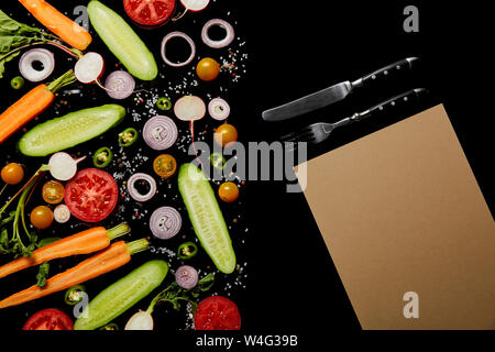 Vista dall'alto di fette di verdure con sale vicino a carta vuota e posate isolati su nero con spazio di copia Foto Stock