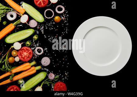 Vista superiore del vuoto piastra rotonda vicino a fette vegetale isolato su nero Foto Stock