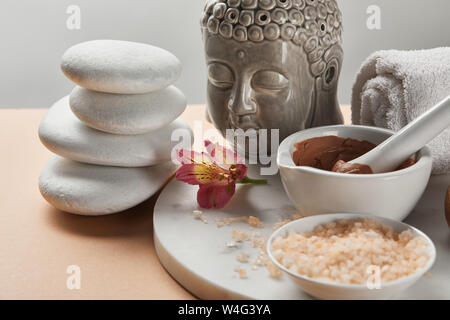 Argilla e sale marino in ciotola vicino a BUDDA STATUETTA e spa pietre sul cerchio di marmo isolato su grigio Foto Stock