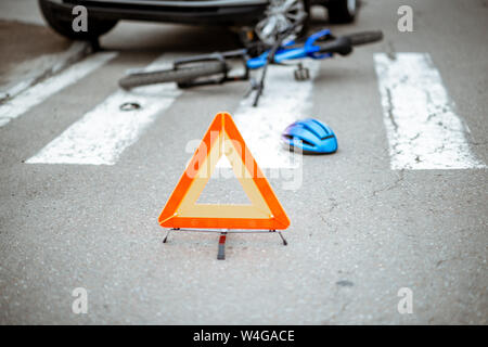 Scena di un incidente stradale con auto e biciclette rotte giacente sul passaggio pedonale. Triangolo di traffico in primo piano Foto Stock