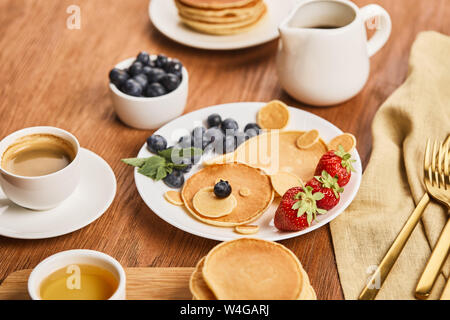 Vista dall'alto di frittelle con le bacche sulla piastra, sciroppo in caraffa, miele e caffè, concetto di orso Foto Stock