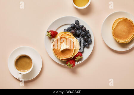 Vista dall'alto di frittelle con frutti di bosco, vicino a tazza di caffè e una ciotola con il miele in rosa Foto Stock