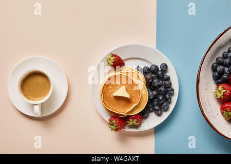 Vista dall'alto di frittelle con le bacche sulla piastra vicino a tazza di caffè Foto Stock