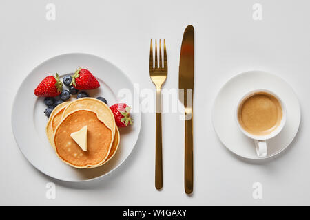 Vista superiore della gustosa prima colazione con pancake, bacche e tazza di caffè vicino a golden posate Foto Stock