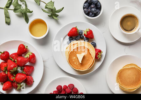 Vista dall'alto di una sana colazione con fragole, mirtilli, lamponi, frittelle, il miele e la tazza di caffè Foto Stock