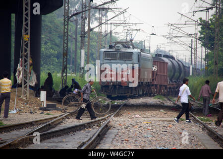 Gruppo di persone che attraversano i binari ferroviari con il treno in background, Delhi, India Foto Stock