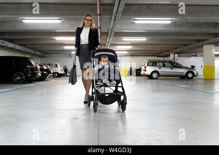 Giovane imprenditrice spingendo un passeggino con baby boy in parcheggio Foto Stock