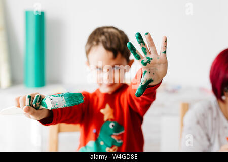 Ragazzo che mostra una spazzola in una mano e l'altra dipinte di verde mentre si fanno i mestieri a casa Foto Stock