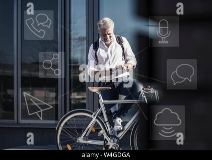 Sorridente imprenditore maturo con bicicletta utilizzando il telefono cellulare per la messaggistica in città Foto Stock