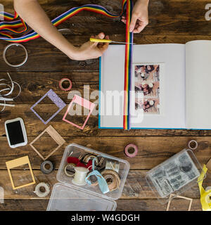 Vista superiore della donna con le mani in mano la decorazione di un album di foto con un nastro di Rainbow Foto Stock