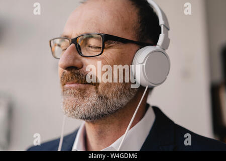 Imprenditore maturo con gli occhi chiusi per ascoltare musica con le cuffie Foto Stock