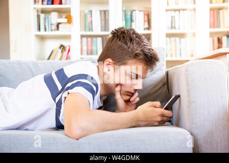 Ragazzo adolescente sdraiato sul divano di casa utilizzando il telefono cellulare Foto Stock