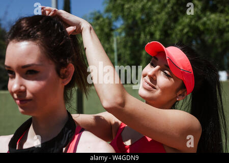 Donna sorridente giocatore di tennis facendo i capelli del suo partner di formazione Foto Stock