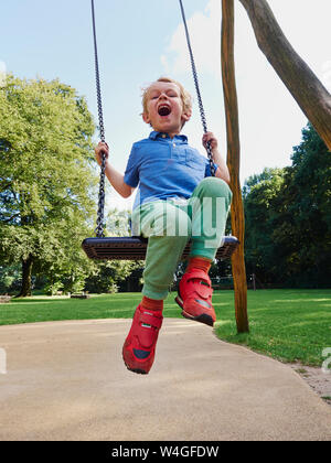 Ritratto di urlando little boy su swing Foto Stock