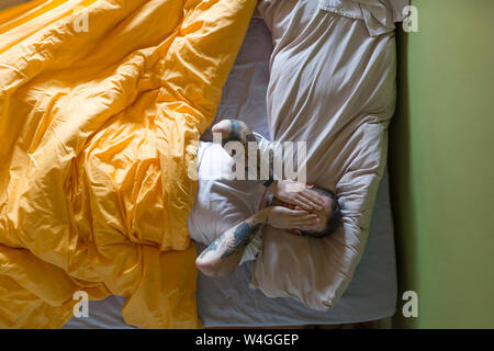 Tatuato uomo disteso nel letto e le mani sugli occhi Foto Stock