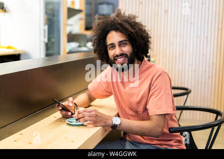 Ritratto di un uomo sorridente con un telefono cellulare seduto presso il bancone di un bar Foto Stock