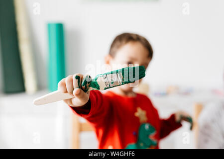 Bambino con una spazzola in mano fare artigianato a casa Foto Stock