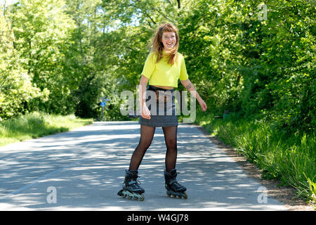 Ritratto di ridere giovane donna con pattini a rotelle in linea Foto Stock