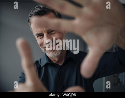 Ritratto di sorridente imprenditore maturo rendendo un dito telaio Foto Stock