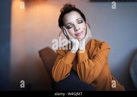 Ritratto di donna sorridente con gli occhi chiusi seduti sul divano di casa Foto Stock