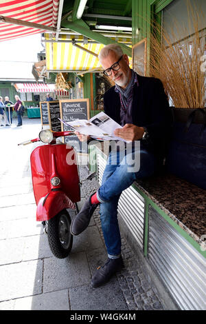 Uomo maturo in attesa presso il mercato, leggendo la brochure Foto Stock