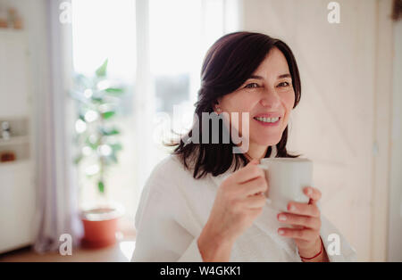 Donna matura in un accappatoio, bere il suo caffè del mattino Foto Stock