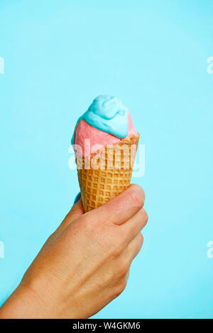 Donna di mano che tiene il cono gelato di fronte a sfondo blu Foto Stock