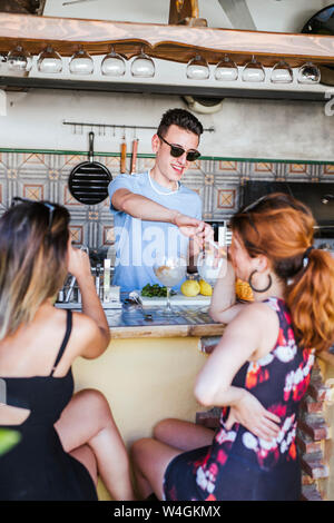 Barman preparare bevande per due donne in un bar Foto Stock