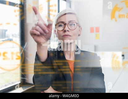 Imprenditrice di toccare la parete di vetro con dati in ufficio Foto Stock