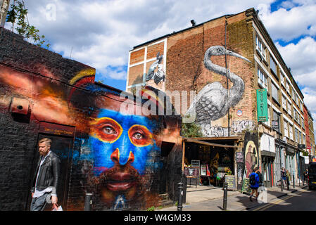 Persone che passano dal muro di graffiti arte a Brick Lane market a Londra, Regno Unito Foto Stock