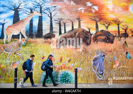 Persone che passano dal muro di graffiti arte a Brick Lane market a Londra, Regno Unito Foto Stock
