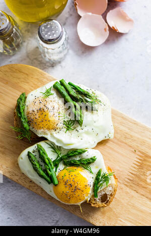 Fette di baguette guarnita con uova fritte e gli asparagi su di una piastra Foto Stock