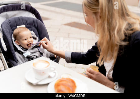 Alimentazione madre Laughing baby boy in passeggino Foto Stock