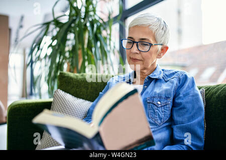 Senior donna seduta sul lettino, la lettura di un libro Foto Stock