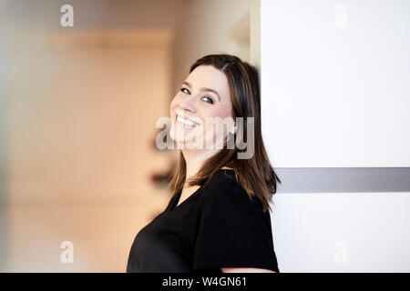 Ritratto di donna sorridente in un ufficio appoggiata contro la parete Foto Stock