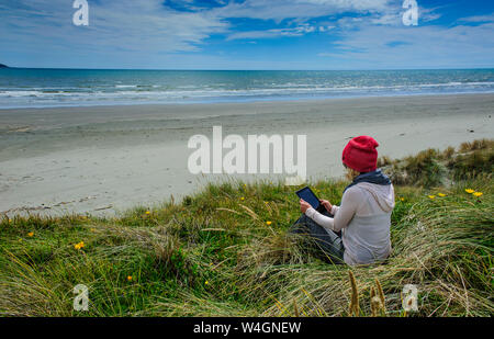 Donna che utilizza tablet a Foxton beach, la Costa di Kapiti, Isola del nord, Nuova Zelanda Foto Stock