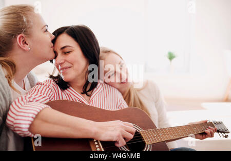 Donna matura con due figlie affettuoso a suonare la chitarra a casa Foto Stock