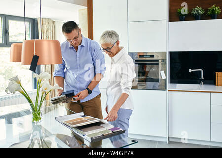 Uomo e donna matura in una cucina store esaminando campioni di materiale Foto Stock