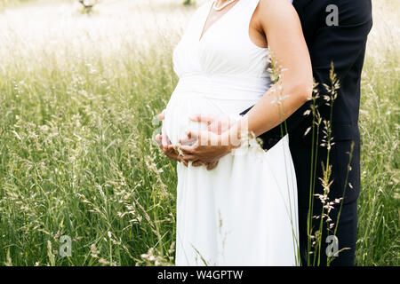 Sposa incinta con il marito holding baby ventre su un prato Foto Stock