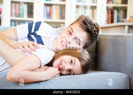 Ritratto di ragazzo adolescente e sua sorella più piccola giacente insieme sul lettino a casa Foto Stock